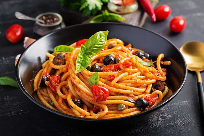 Spaghetti alla puttanesca – italienisches Nudelgericht mit Tomaten, schwarzen Oliven, Kapern, Sardellen und Basilikum.